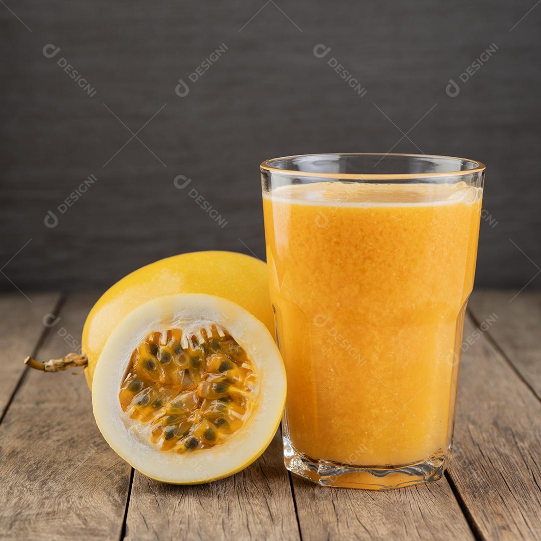 Suco de maracujá em um copo com frutas sobre a mesa de madeira.