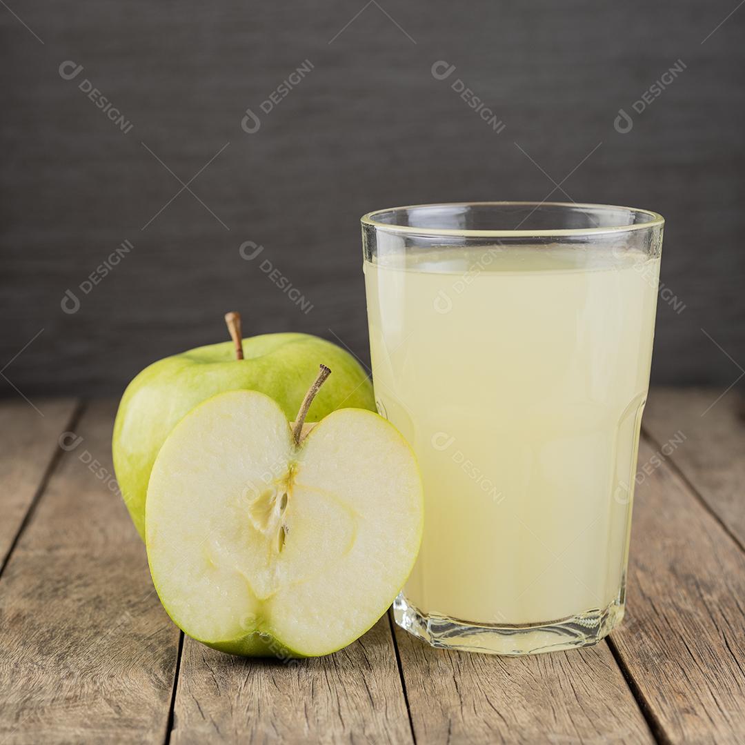 Suco de maçã verde em um copo com frutas sobre a mesa de madeira.