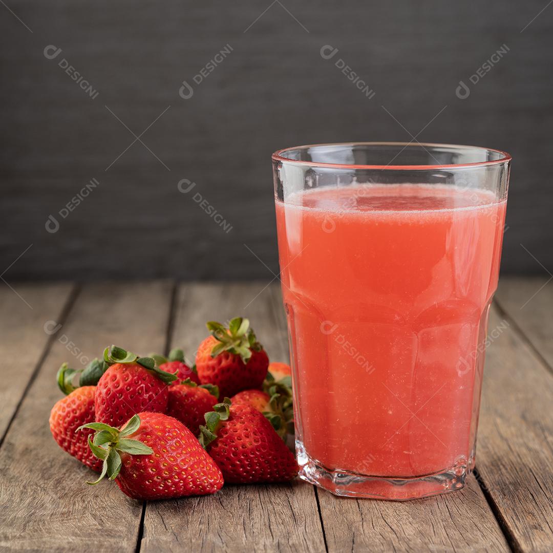 Suco de morango em um copo com frutas sobre a mesa de madeira.