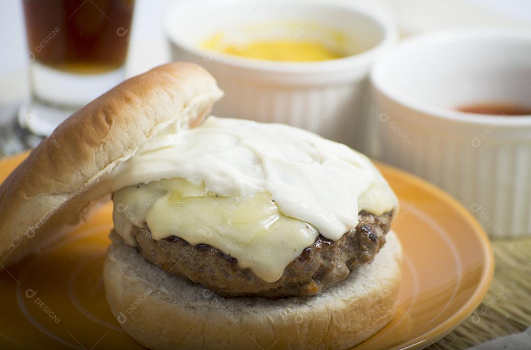 Cheeseburger com maionese, mostarda e ketchup em tigelas brancas e copo de refrigerante.