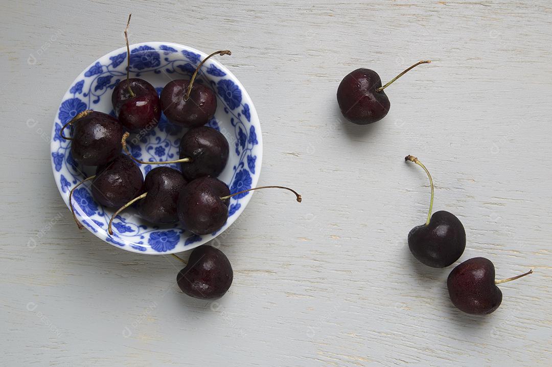 Cerejas pretas em uma tigela vintage branca e azul sobre a mesa de madeira.