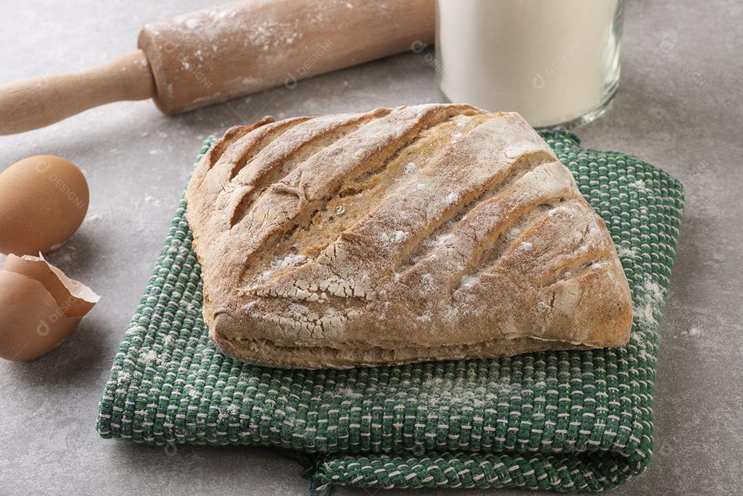 Pão inteiro sobre pano com farinha, ovos e rolo