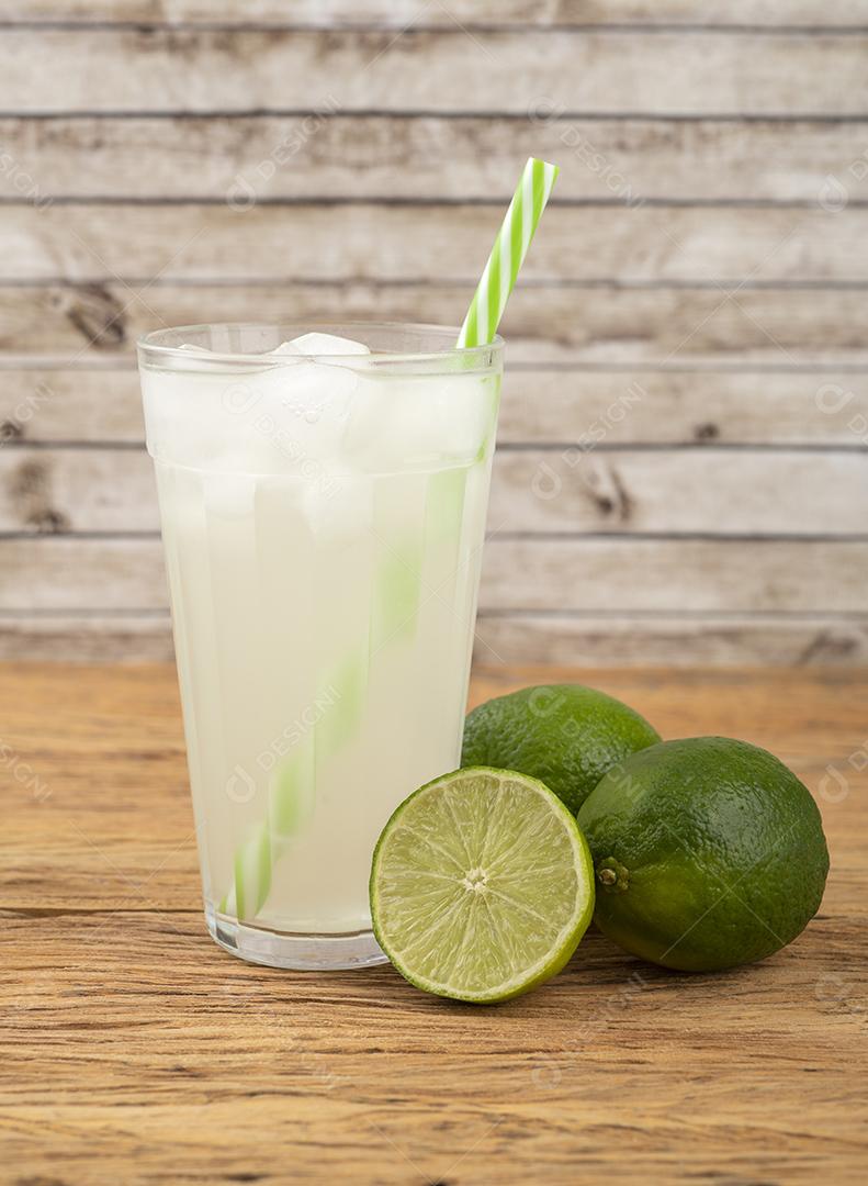 Suco de limão verde em um copo com gelo e frutas sobre aba de madeira
