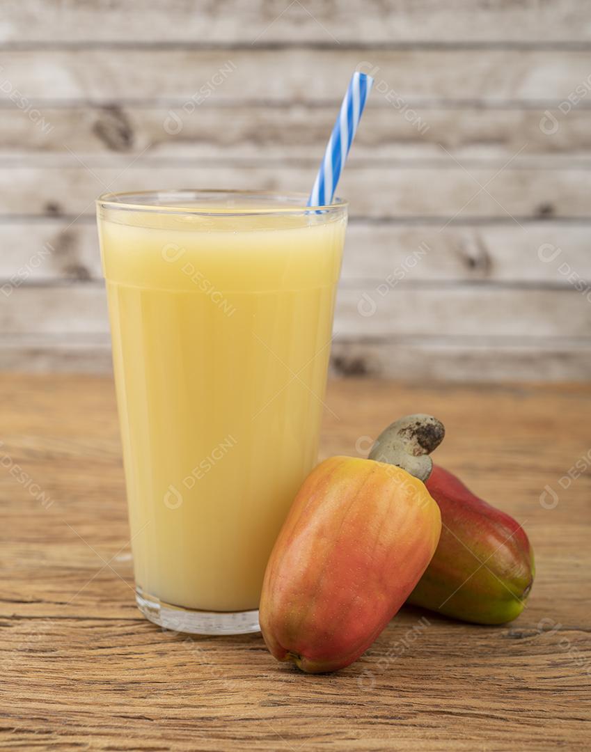 Suco de caju em um copo com frutas sobre mesa de madeira