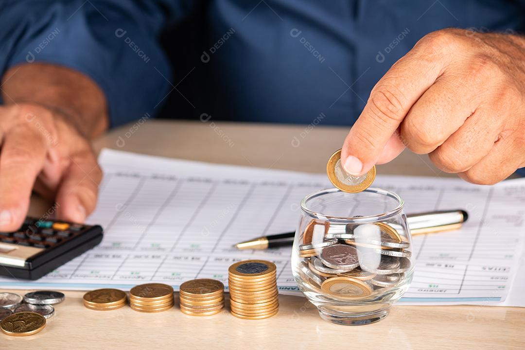 Empresário segurando moedas e colocando em pote de vidro. Poupança