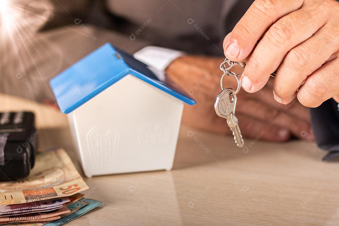 Homem de negócios segurando chave com casa pequena na mesa. habitação