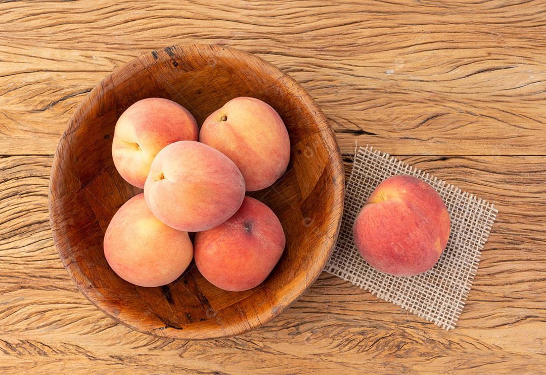 Pêssegos em uma tigela sobre mesa de madeira