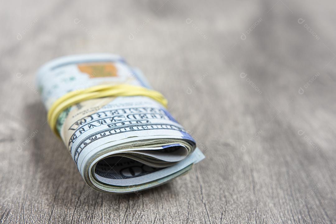 Notas de cem dólares embaladas em um elástico sobre mesa de madeira