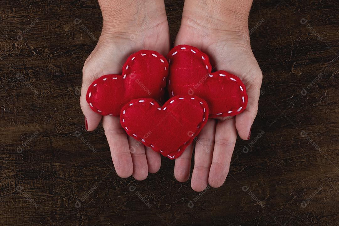 Mão feminina segurando corações vermelhos em fundo rústico