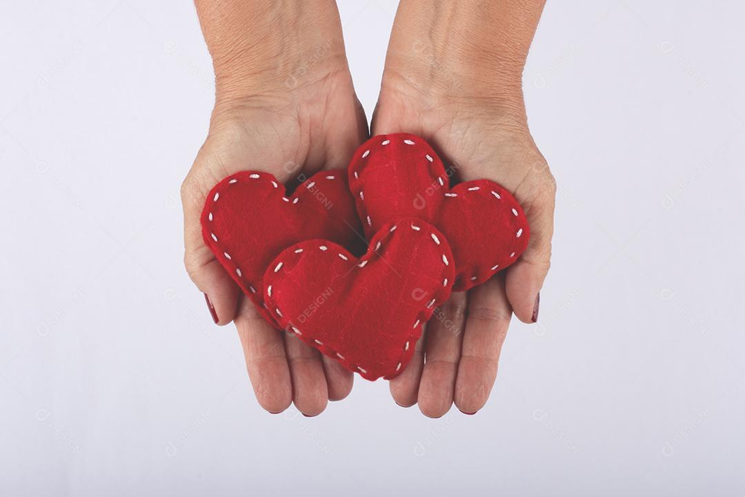 Mão feminina segurando corações vermelhos sobre fundo branco.