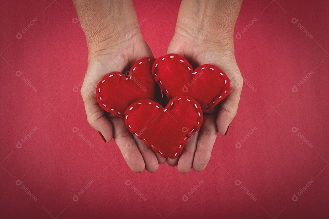 Mão feminina segurando corações vermelhos sobre fundo vermelho.
