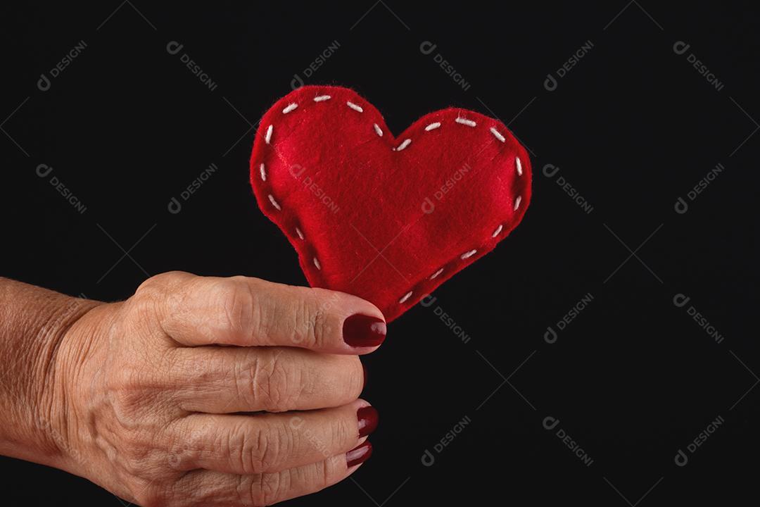 Mão feminina segurando um coração vermelho sobre fundo preto.