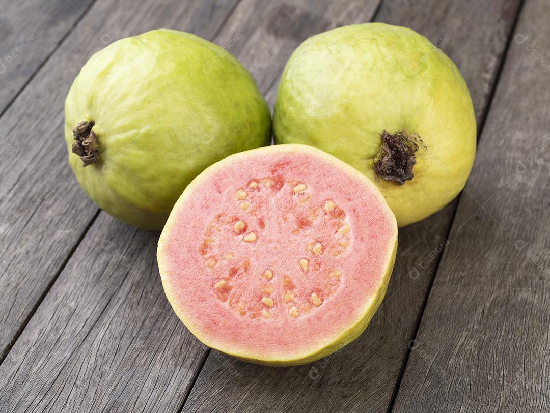 Duas goiabas com frutas fatiadas sobre mesa de madeira