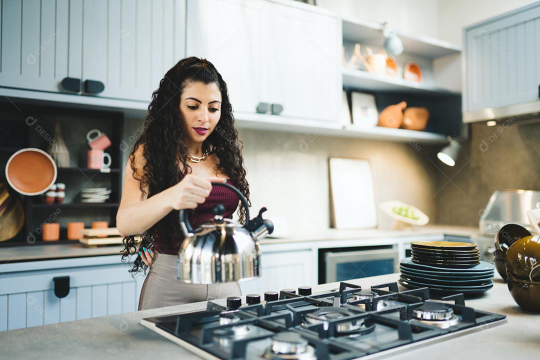 Jovem mulher latina em casa preparando chá na cozinha.