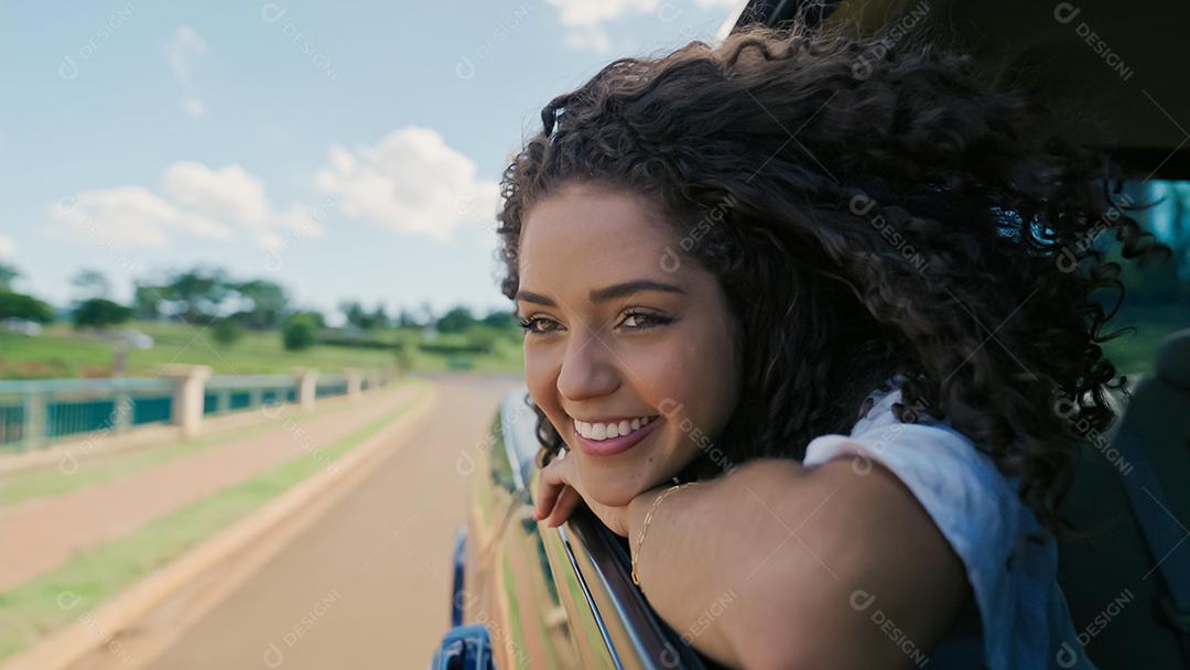 Mulher latina na janela do carro. Viagem de carro. Cabelos cacheados ao vento