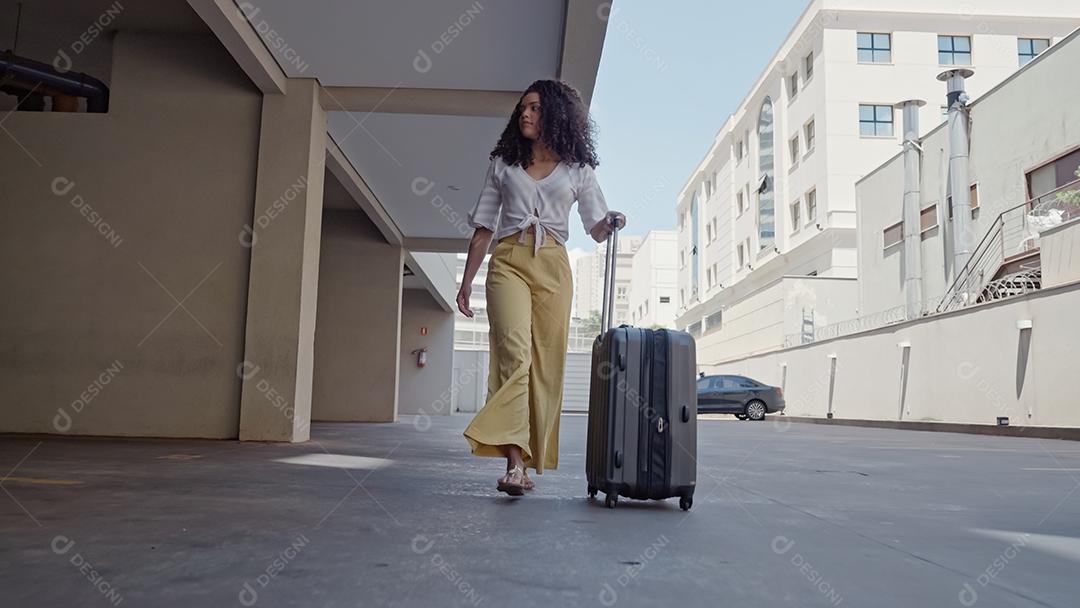Jovem turista latina caminha com uma mala sobre rodas