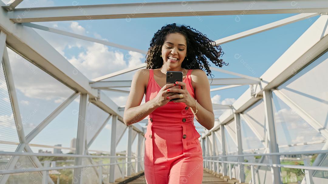 Jovem mulher latina de cabelo encaracolado andando usando o celular. Mensagens de texto