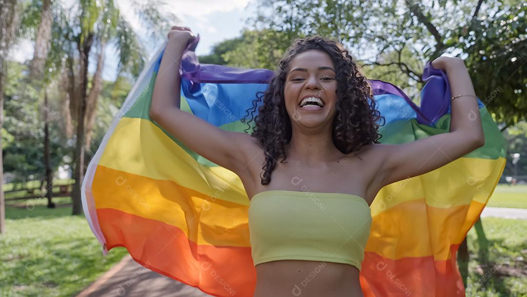 Mulher jovem de cabelo encaracolado cobrindo com bandeira do orgulho lgbt