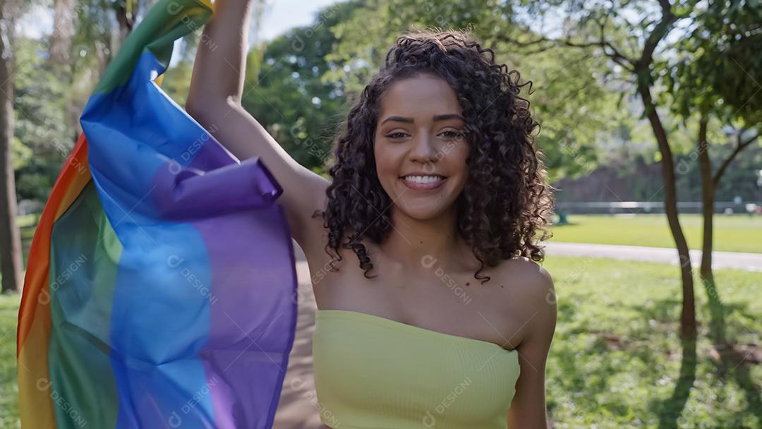 Mulher jovem de cabelo encaracolado cobrindo com bandeira do orgulho lgbt