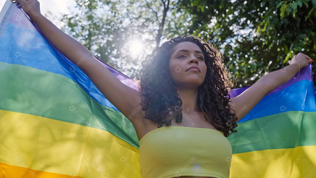 Mulher jovem de cabelo encaracolado cobrindo com bandeira do orgulho lgbt