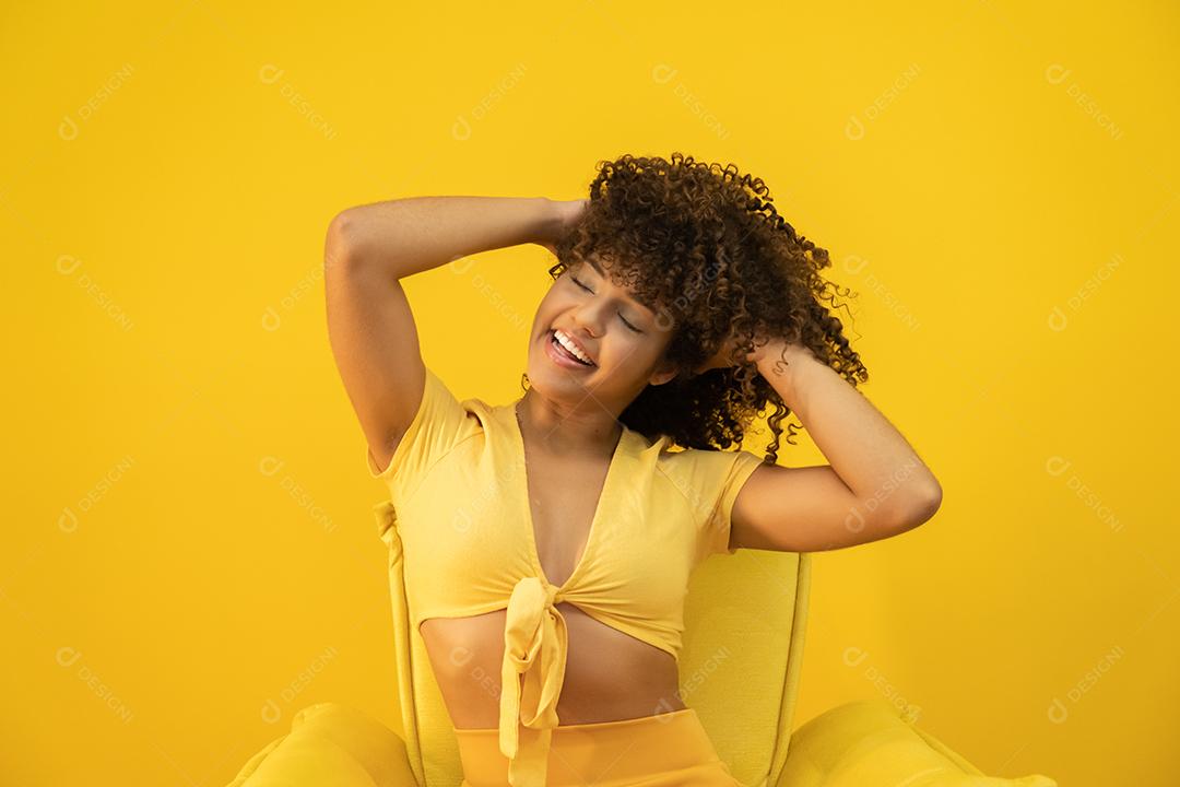 Feliz rindo mulher africana americana com seu cabelo encaracolado em fundo amarelo.