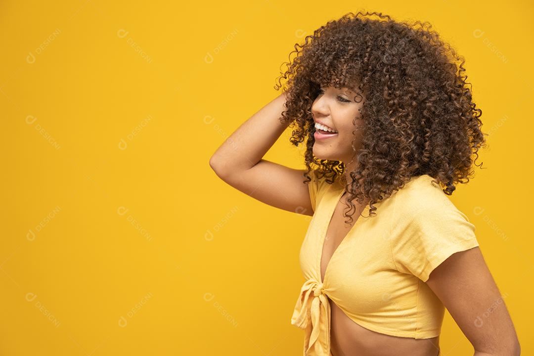 Feliz rindo mulher africana americana com seu cabelo encaracolado em fundo amarelo.