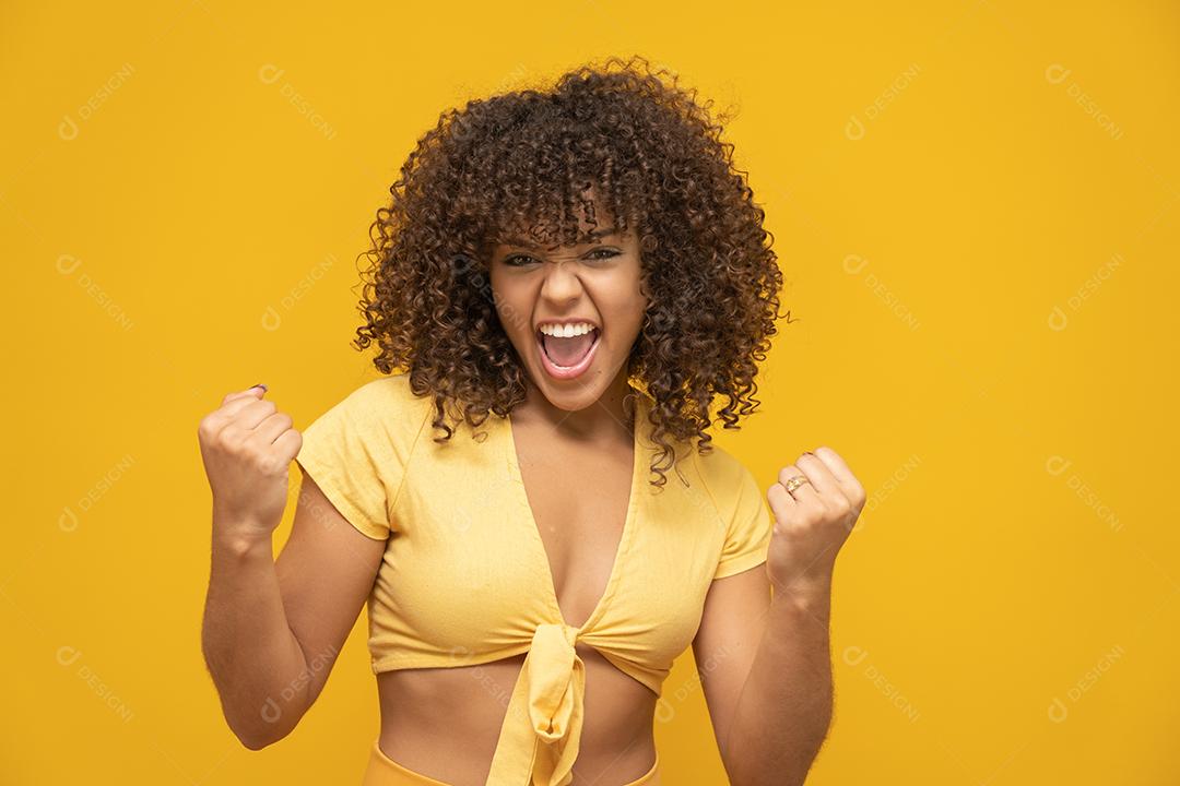 Menina linda morena de cabelo encaracolado feliz regozijando-se dizendo sim sobre fundo amarelo