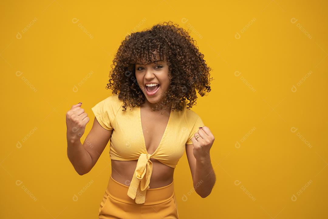Menina linda morena de cabelo encaracolado feliz regozijando-se dizendo sim sobre fundo amarelo