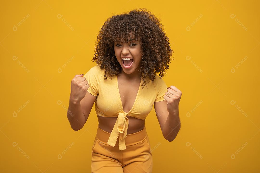 Menina linda morena de cabelo encaracolado feliz regozijando-se dizendo sim sobre fundo amarelo
