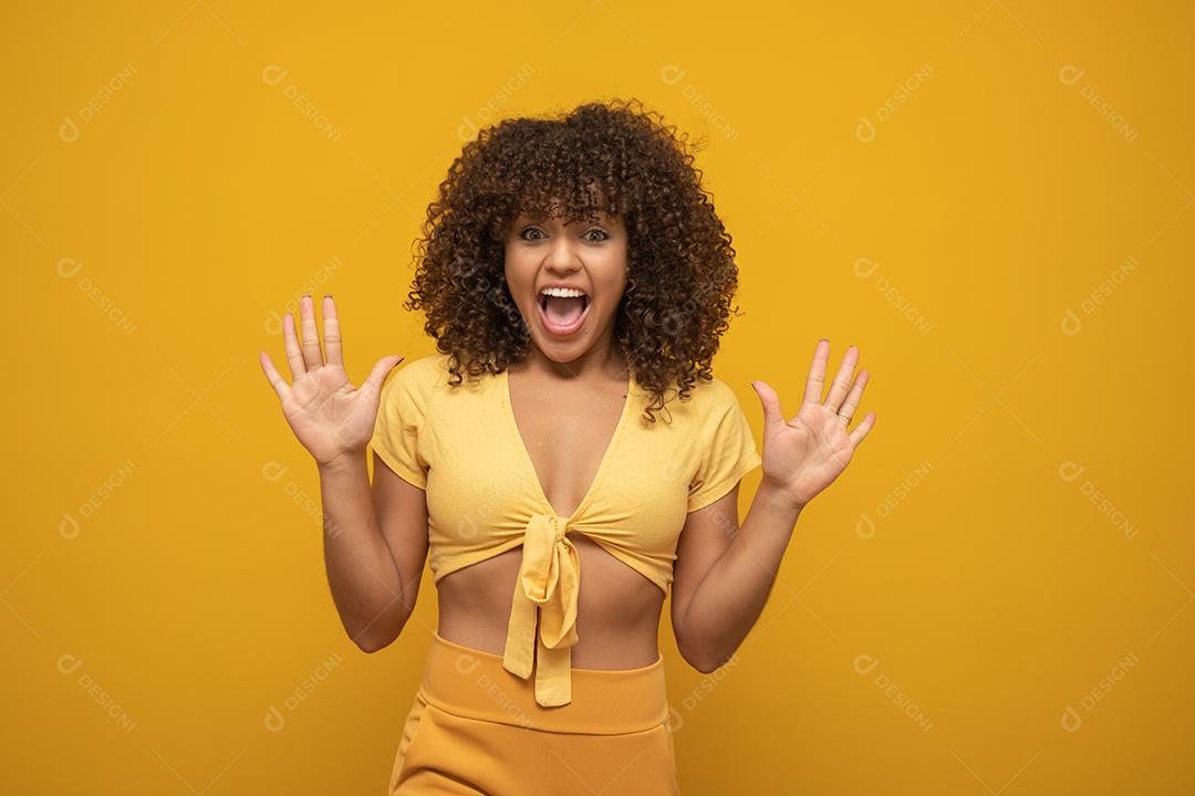 Menina com uma expressão de surpresa no rosto com os braços para cima. Fundo amarelo.
