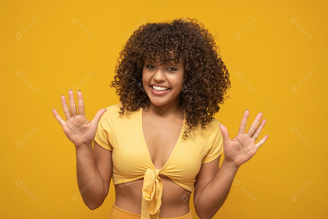 Menina com uma expressão de surpresa no rosto com os braços para cima. Fundo amarelo.