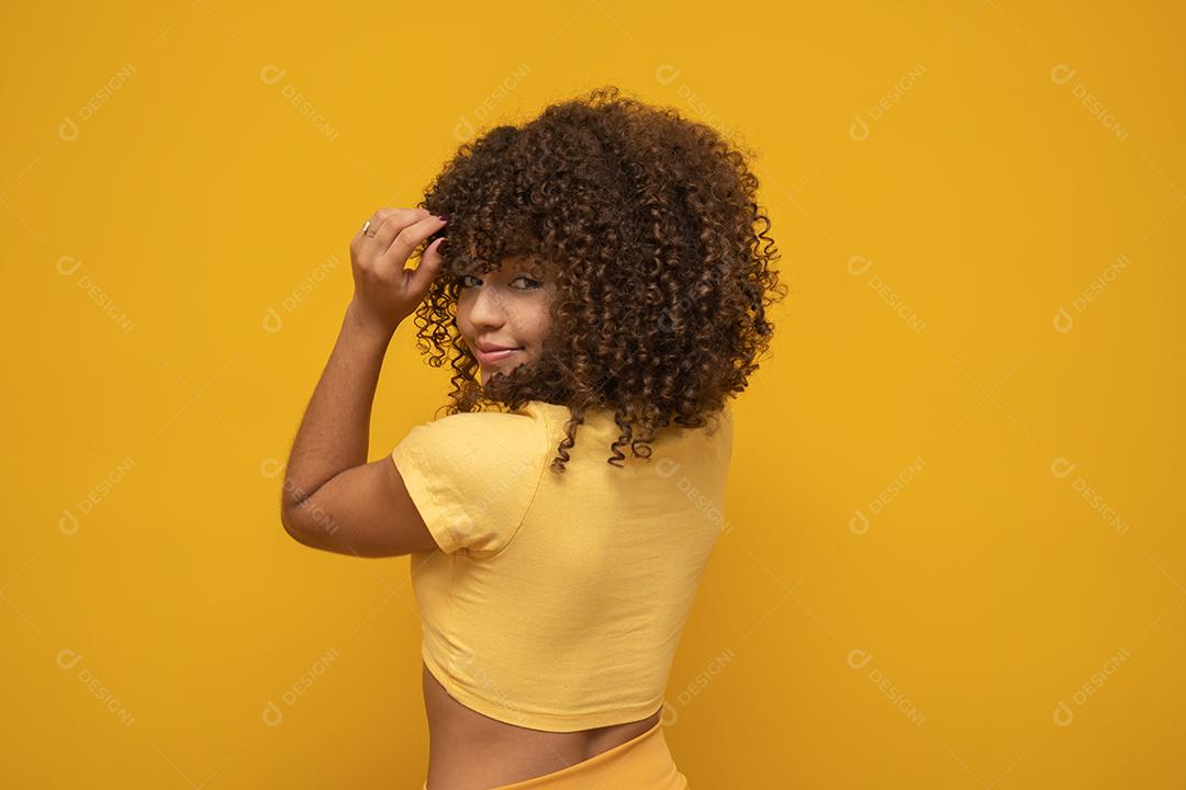 Mulher africana americana para trás com seu cabelo encaracolado em fundo amarelo. Rindo