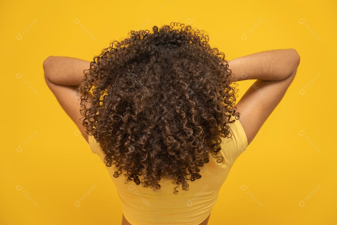 Mulher africana americana para trás com seu cabelo encaracolado em fundo amarelo.