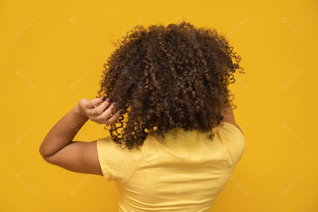 Mulher africana americana para trás com seu cabelo encaracolado em fundo amarelo.