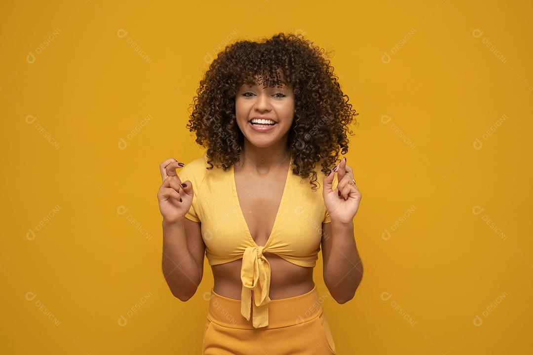 Retrato de uma jovem sorridente com longos cabelos cacheados morenos em pé sobre fundo amarelo