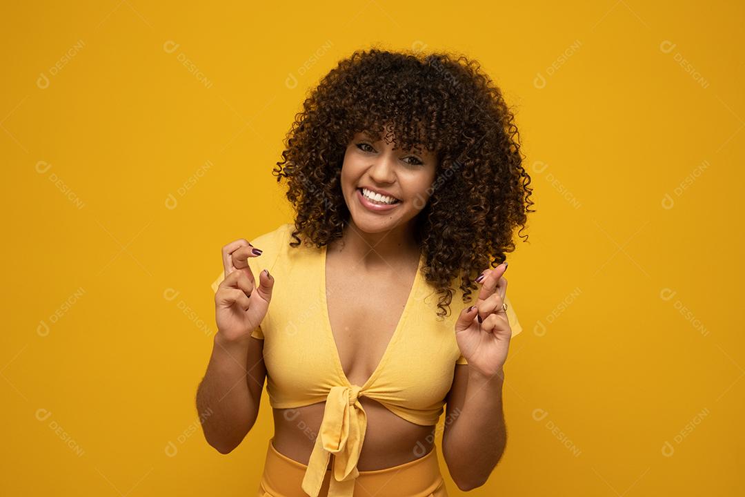 Retrato de uma jovem sorridente com longos cabelos cacheados morenos em pé sobre fundo amarelo