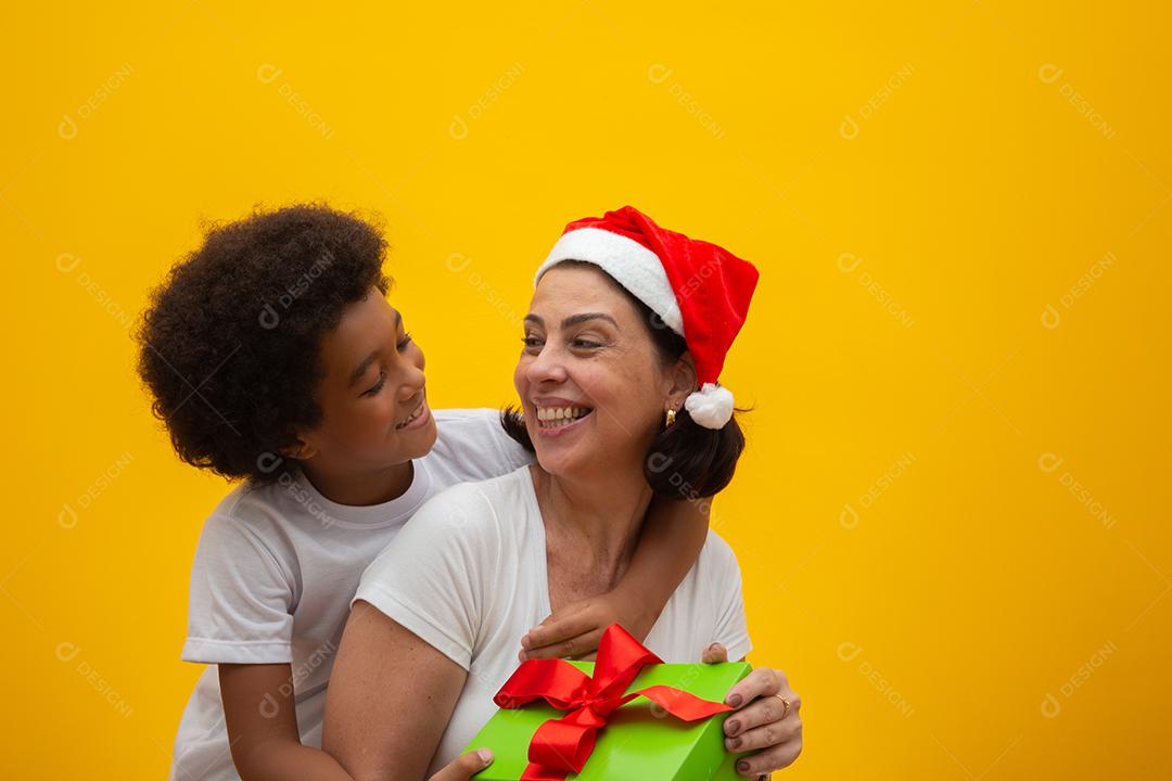 Mãe branca com filho negro trocando presentes na véspera de Natal. Conceito de filho adotivo. Respeito social, cor da pele, inclusão.