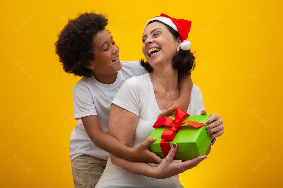 Mãe branca com filho negro trocando presentes na véspera de Natal. Conceito de filho adotivo. Respeito social, cor da pele, inclusão.