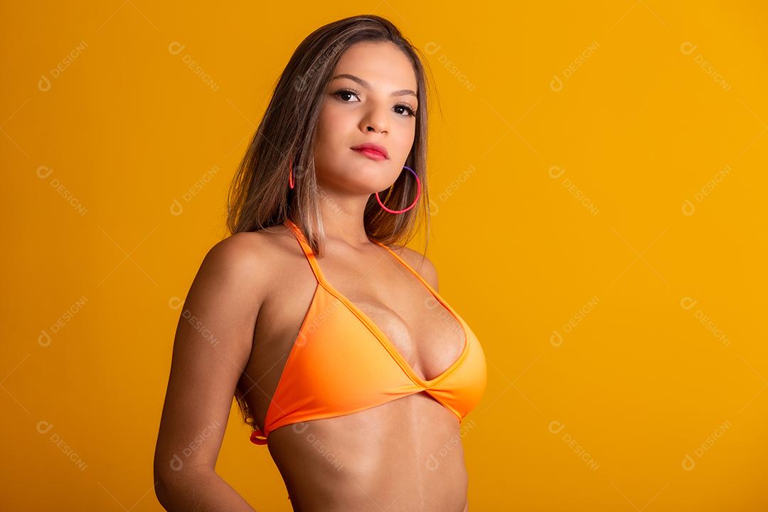 Garota atraente em um biquíni laranja, chapéu, boca aberta emocionalmente em um fundo amarelo