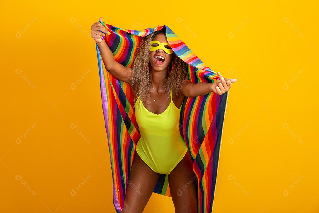 Mulher jovem de cabelo encaracolado fantasiada curtindo a festa de carnaval cobrindo com a bandeira do orgulho lgbt