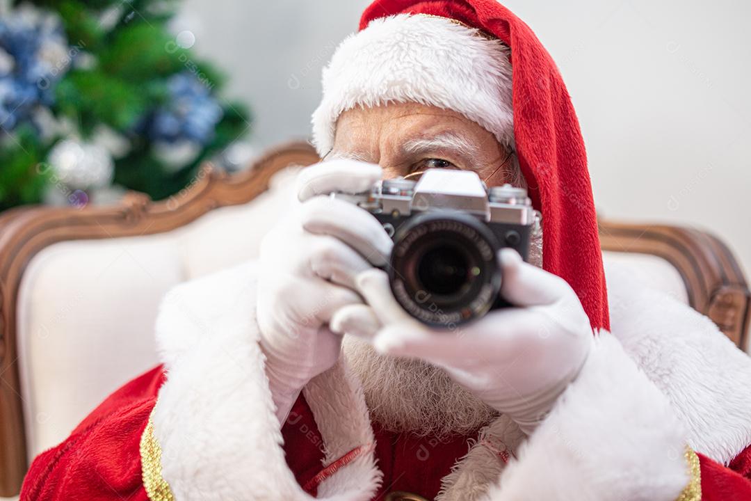 Papai Noel segurando a câmera vintage. Retrato isolado em fundo amarelo.