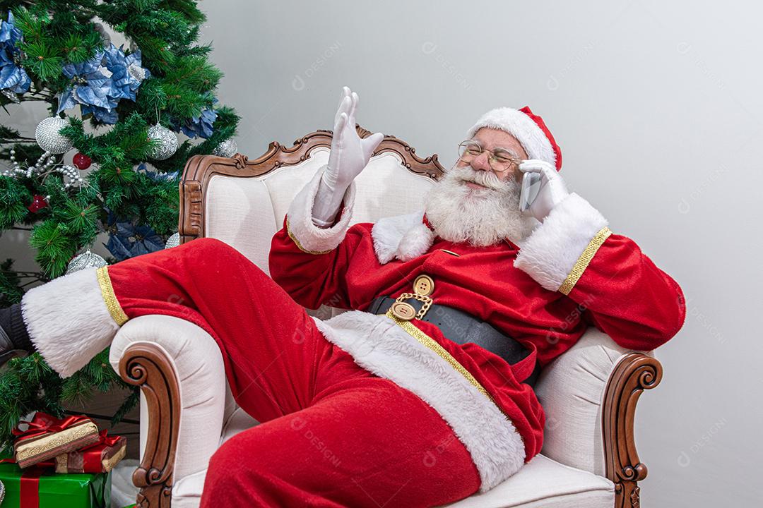Papai Noel usando um smartphone. Falando ao telefone com a criança. Analisando pedidos de Natal.