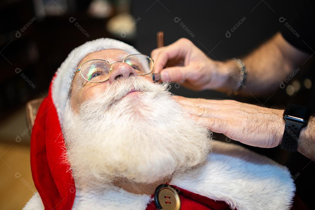 Papai Noel se barbeando na barbearia. Olhando no espelho