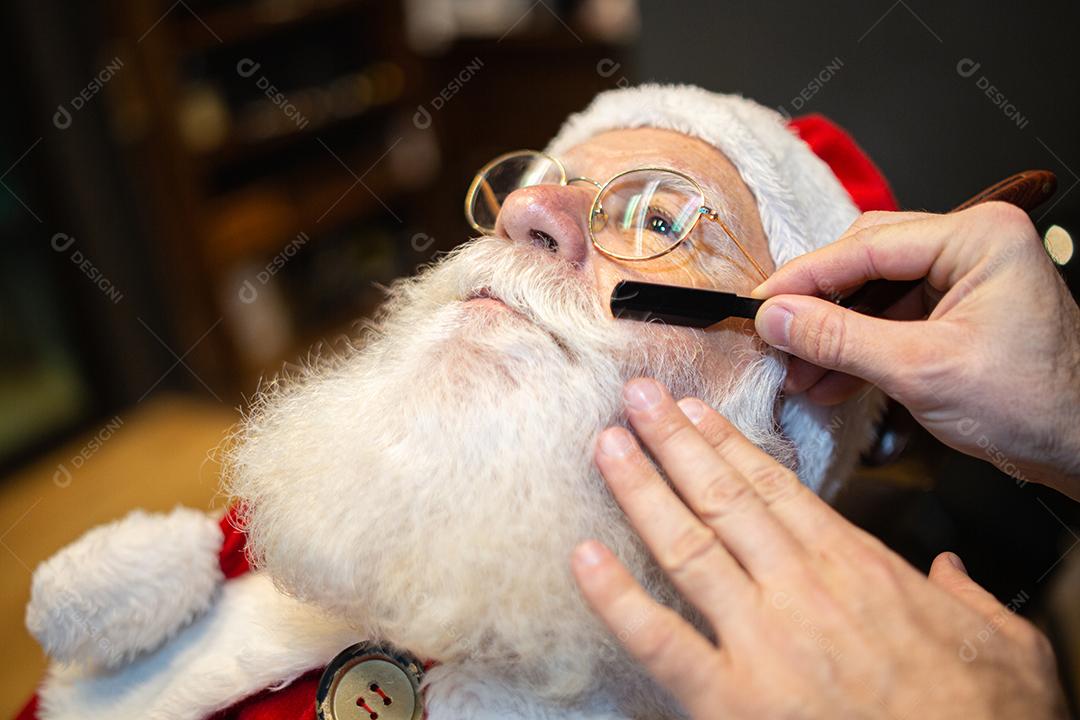 Papai Noel se barbeando na barbearia. Olhando no espelho