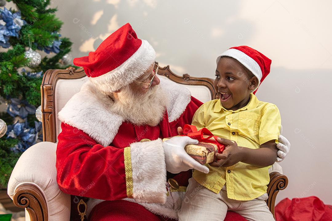 Papai Noel entregando uma caixa de presente para um menino africano. Abraçar