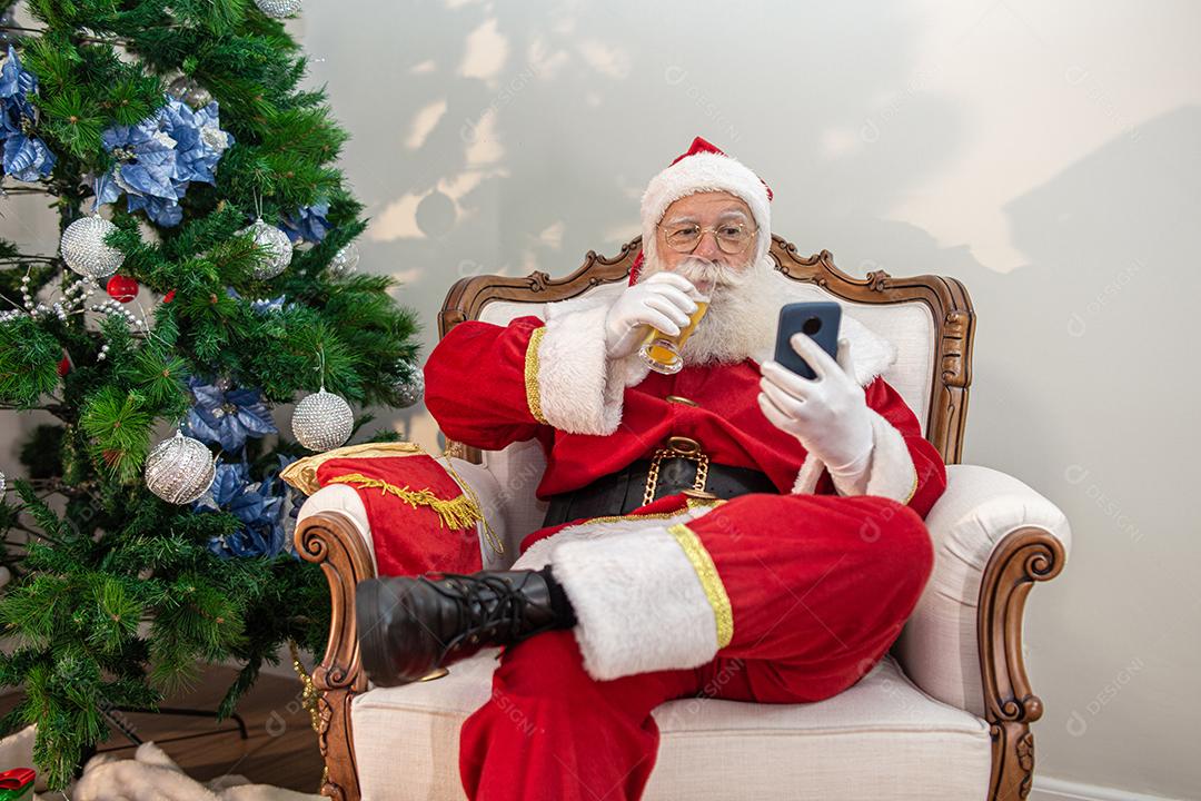 Papai Noel bebendo um copo de cerveja enquanto usava o celular.