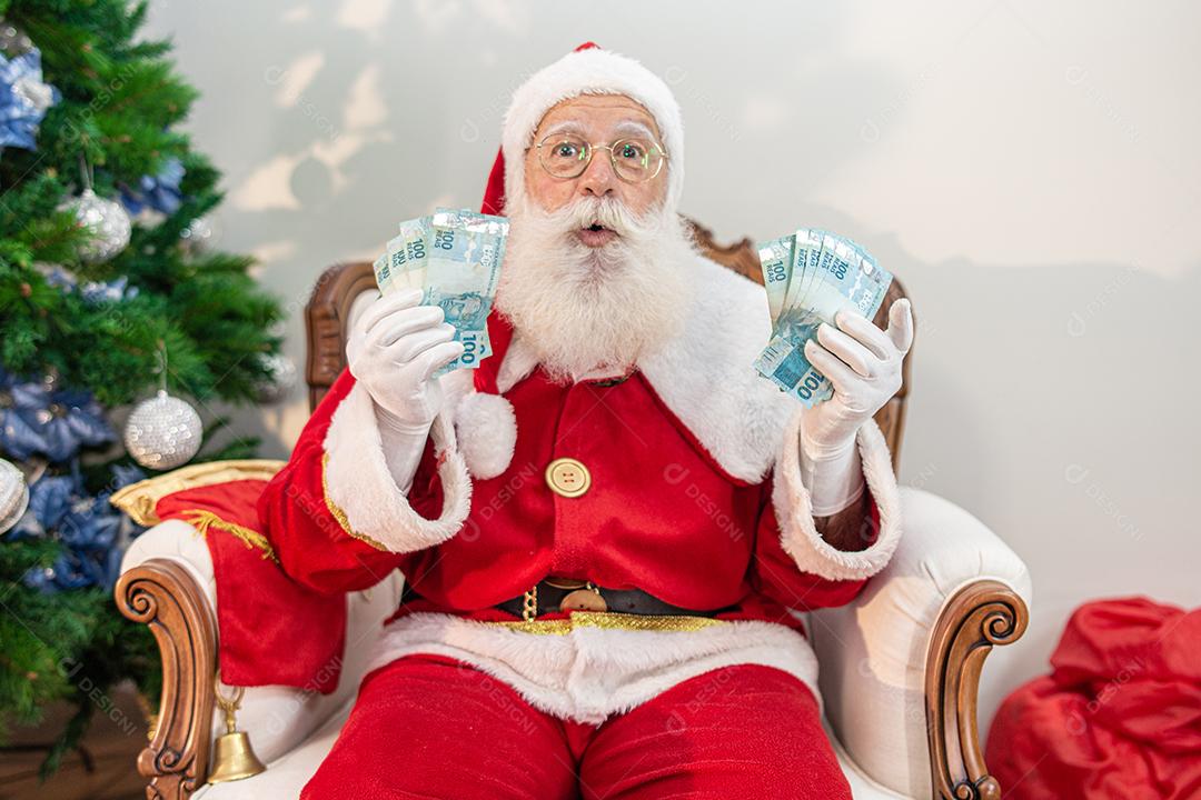 Papai Noel contando contas de dinheiro brasileiras. Notas reais. 100 Reais