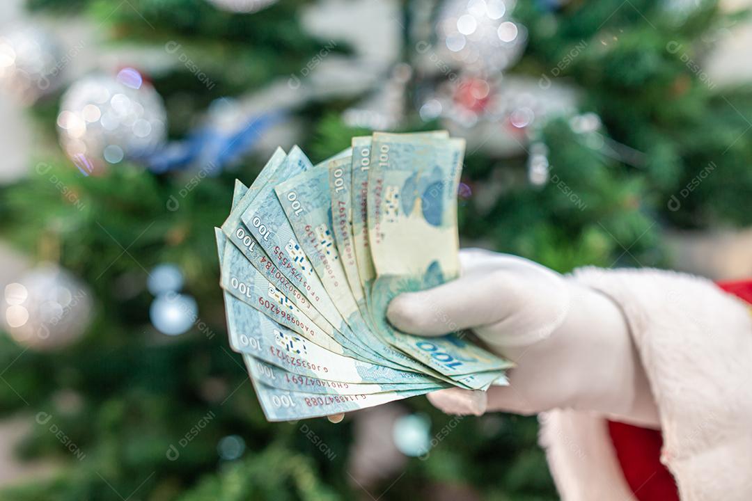 Papai Noel contando contas de dinheiro brasileiras. Notas reais. 100 Reais