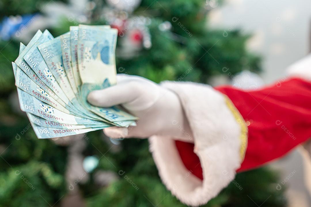 Papai Noel contando contas de dinheiro brasileiras. Notas reais. 100 Reais