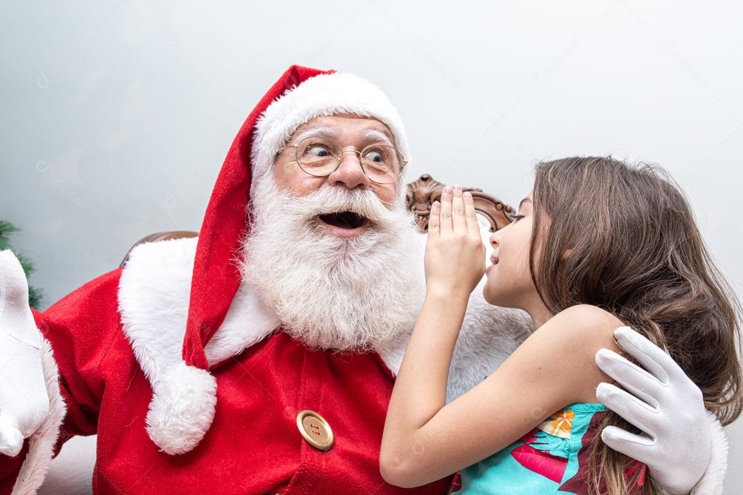Menina sussurrando no ouvido do Papai Noel. Contando um segredo. Revelar